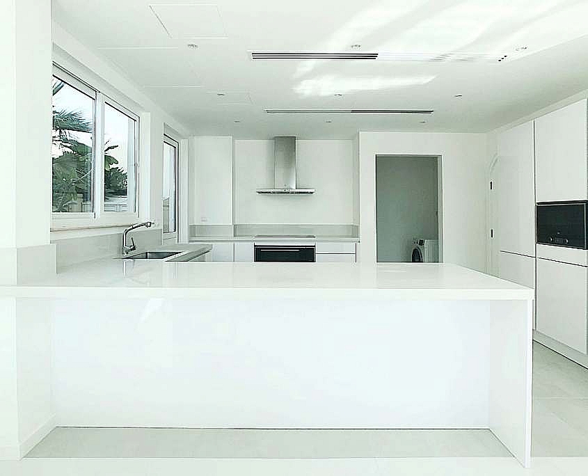 Contemporary all white kitchen renovation in Dubai featuring seamless countertops and island possibly Corian embodying popular modern design